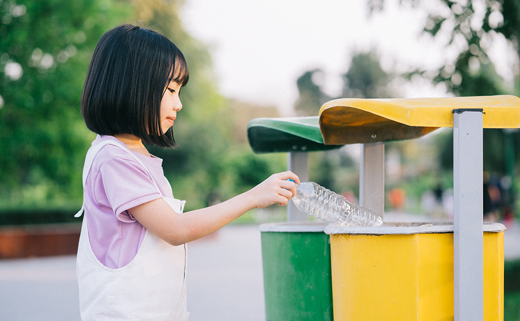 Image of Asian little girl puts used plastic bottles in the trash